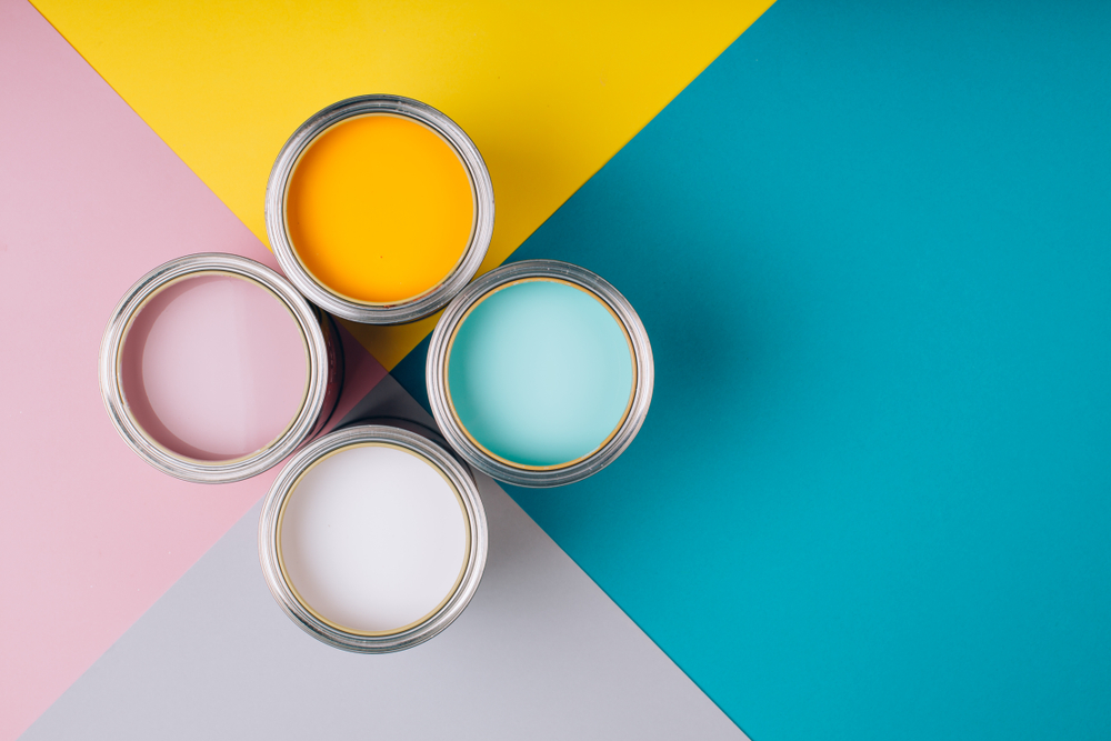 Een visueel feest van kleuren: het aanbrengen van renovlies in diverse tinten op een muur. Kleurrijke verfpotten en behangstalen zijn zorgvuldig gerangschikt op een tafel, illustrerend hoe zelf renovlies aanbrengen de sleutel is tot een levendige en stijlvolle interieurtransformatie.