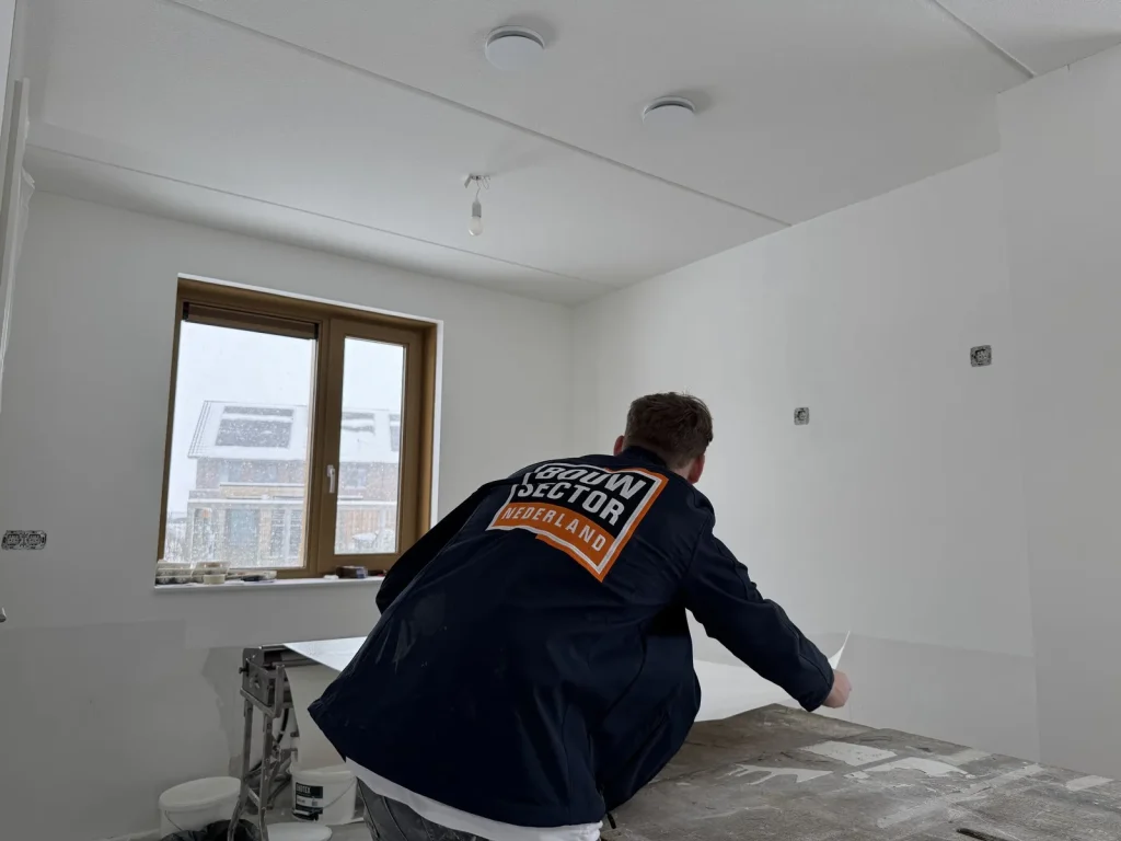 Behanger van Bouwsector Nederland pakt een baan renovlies van de plaktafel bij het raam