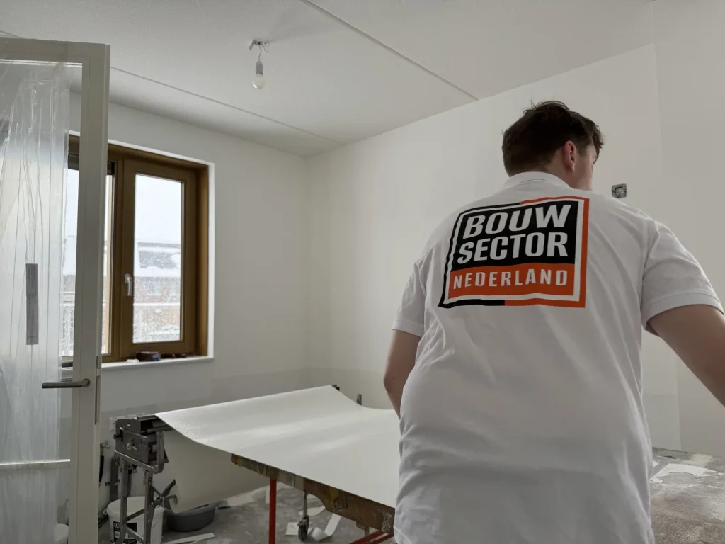 Behanger van Bouwsector Nederland trekt een baan renovlies over de plaktafel richting de wand
