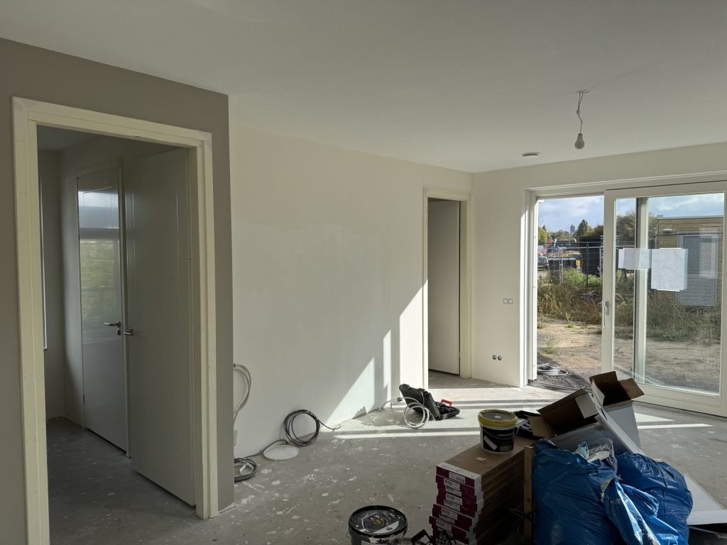 Nieuwbouwwoonkamer tijdens de afwerking met verfemmers, kabels en dozen materiaal op de vloer