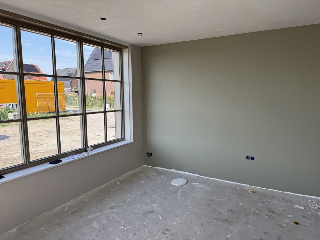Egaal gesausde grijsgroene wand in een nieuwbouwkamer met een groot raam