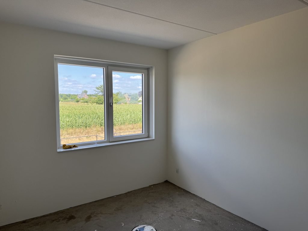 Lege slaapkamer met lichte, gladde wanden en een raam met uitzicht op een maisveld