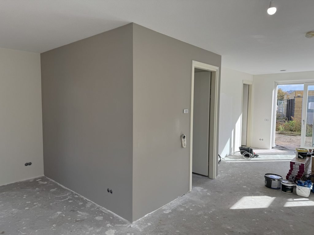 Pas gesausde grijze wand in een nieuwbouwwoning met verfemmers op de betonvloer