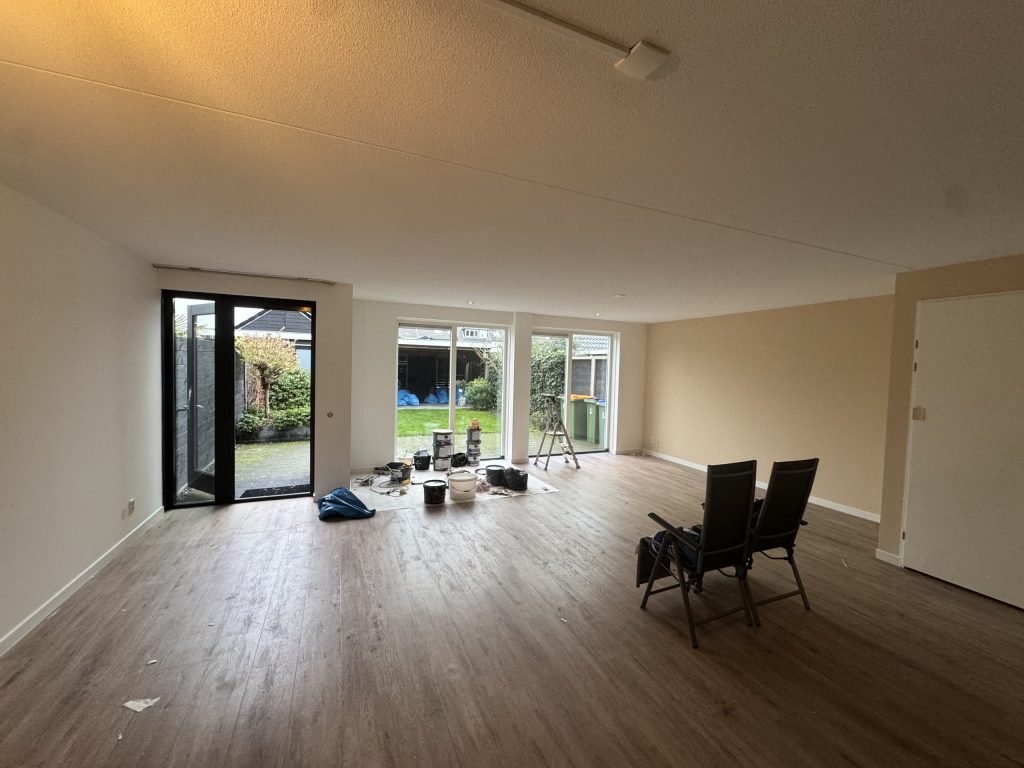 Ruime woonkamer met lichte wanden, een houten vloer en verfspullen bij de tuindeuren