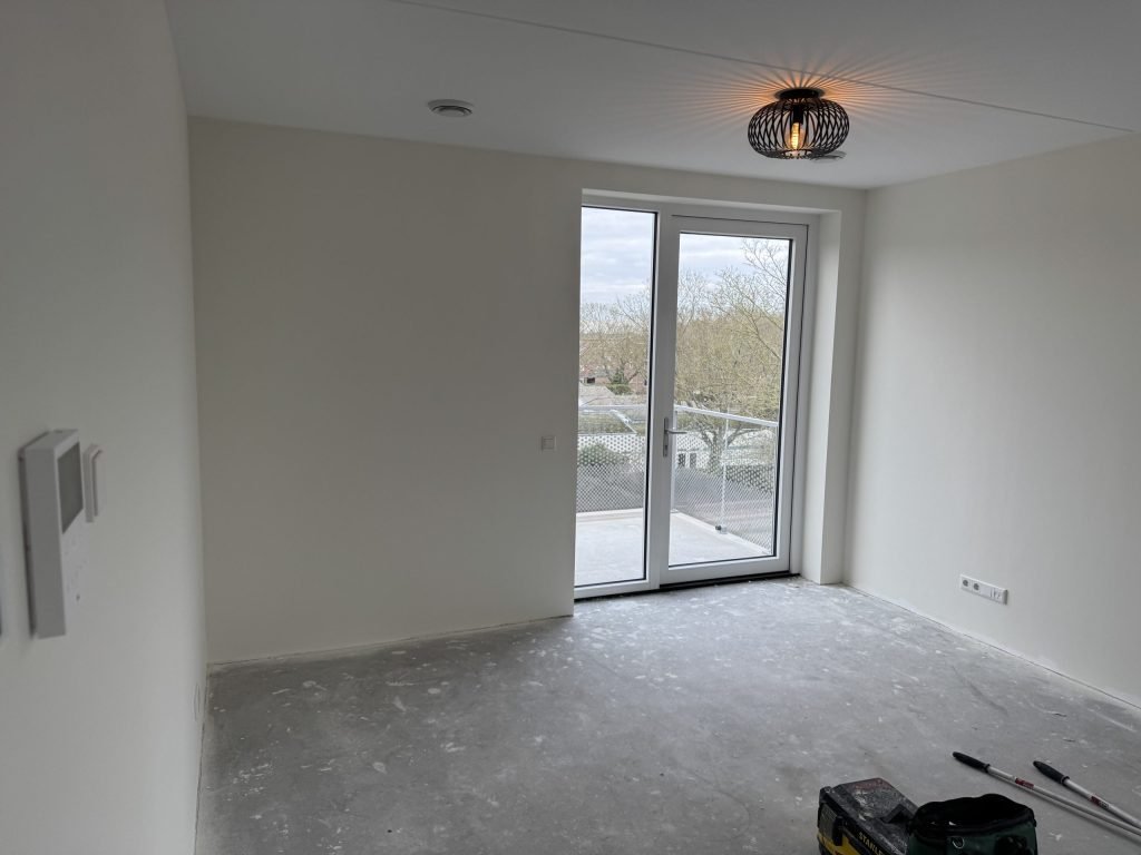 Lege nieuwbouwkamer met balkondeuren, kort na de oplevering, met verfrollers op de vloer