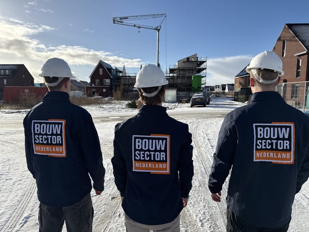 Drie vakmensen van Bouwsector Nederland met witte helm en werkjas op een besneeuwde nieuwbouwplaats